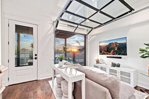 A modern living room with a glass ceiling, a large TV, and a balcony with a sunset view. - Spacious 5-bedroom house w/Elevator and Game room!! (Nashville)