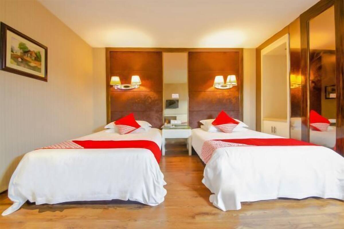 Ein Hotelzimmer mit zwei Einzelbetten, jeweils mit weißer Bettwäsche und roten Kissen. An jeder Seite des Bettes befindet sich eine Wandlampe.