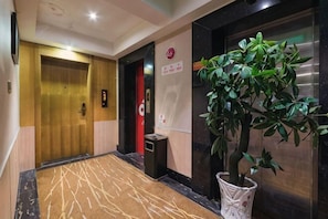 En hotellobby med en trädør, en receptionsdisk, en plante og en elevator.