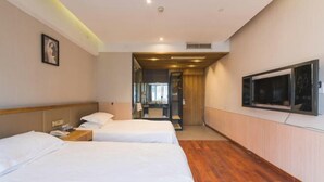 Une chambre d’hôtel avec deux lits, un plancher en bois, un téléviseur fixé au mur et une salle de bain visible à travers une porte ouverte.