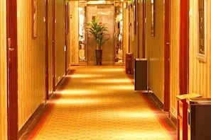 A hotel hallway with wooden paneling, a patterned carpet, and a potted plant. - The First Time Hotel (Yueqing)