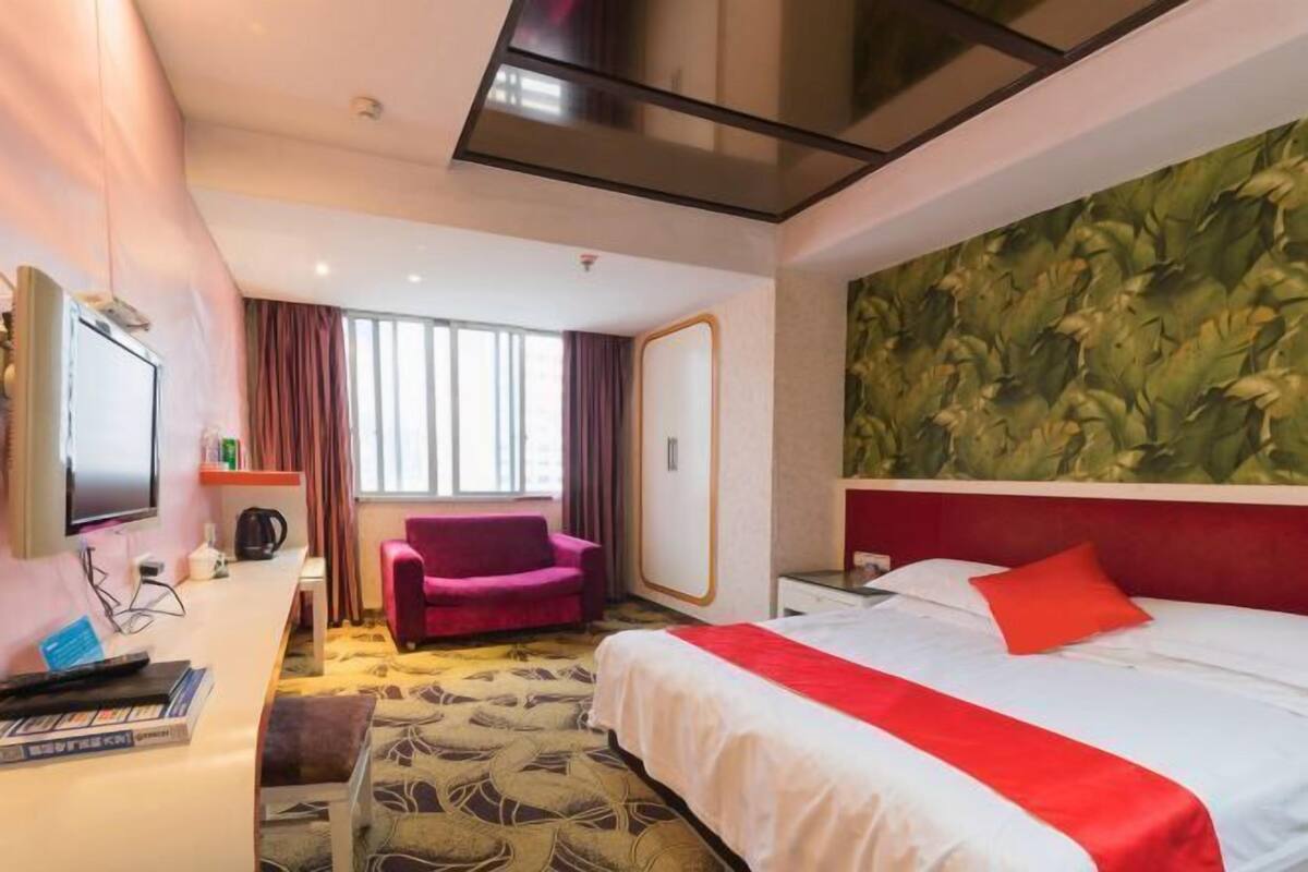 Ein Hotelzimmer mit Bett, Schreibtisch, Stuhl, Fernseher und einem Fenster mit Vorhängen.
