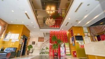 A hotel lobby with a reception desk, seating area, and a staircase leading to upper floors.