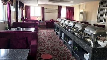 Comedor de hotel con piso de moqueta roja, diversas opciones de asientos como cabinas y mesas, y un sistema de buffet con electrodomésticos de acero inoxidable.