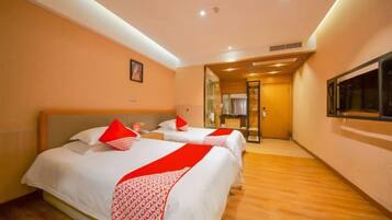 A hotel room with two beds, a wooden floor, a window, and a door leading to a hallway.