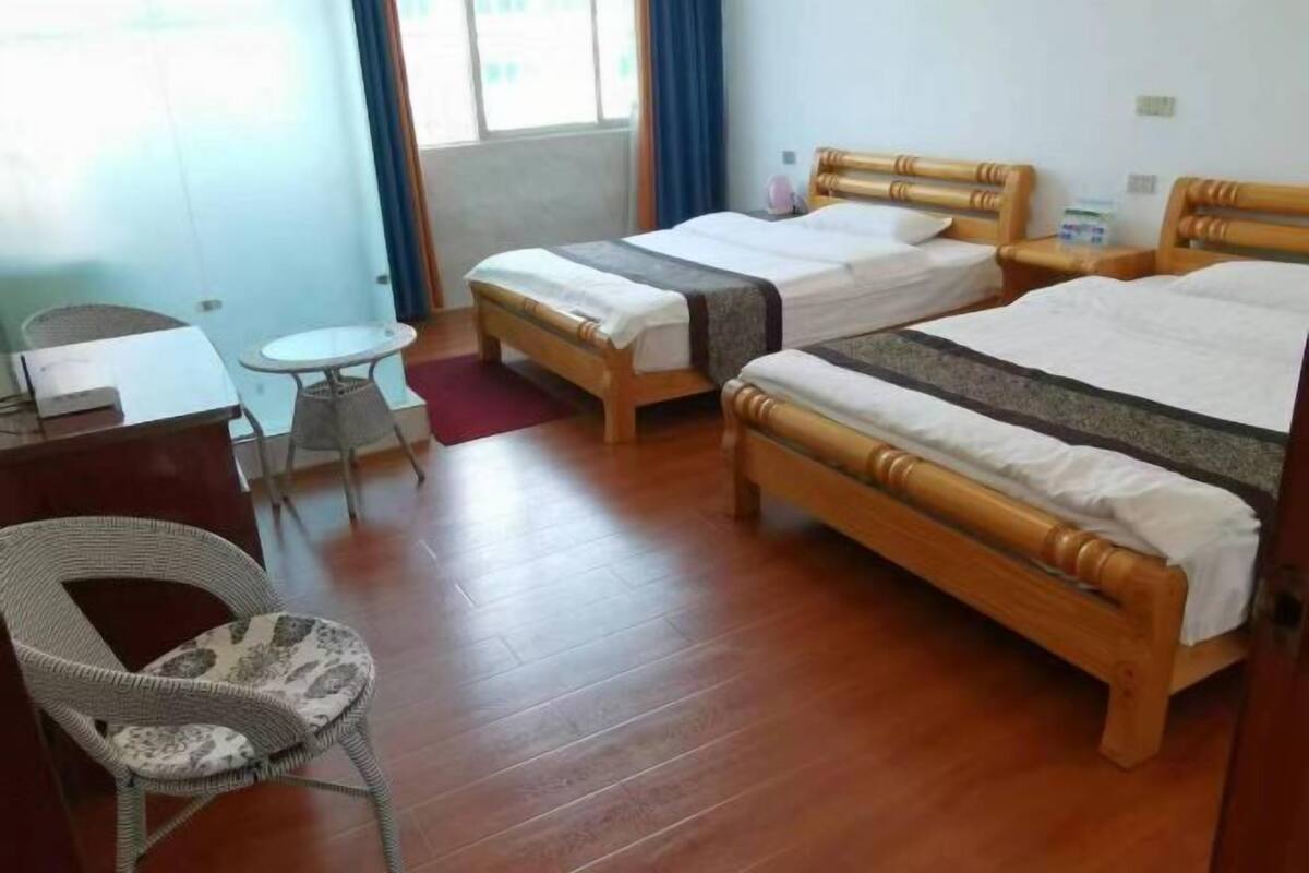 Habitación de hotel con dos camas de madera, una mesita redonda pequeña, una silla de mimbre y un escritorio con una computadora.