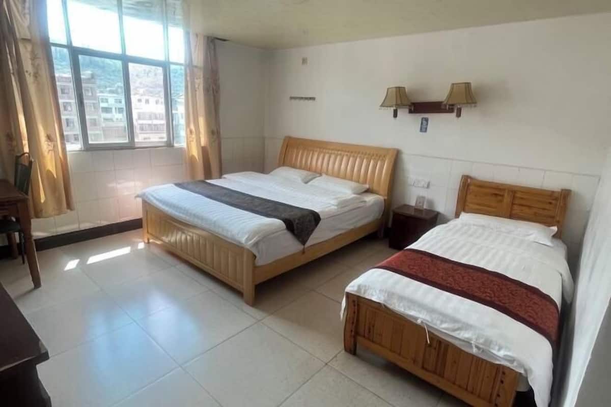 Habitación de hotel con dos camas de madera, un escritorio y un ventanal con cortinas.