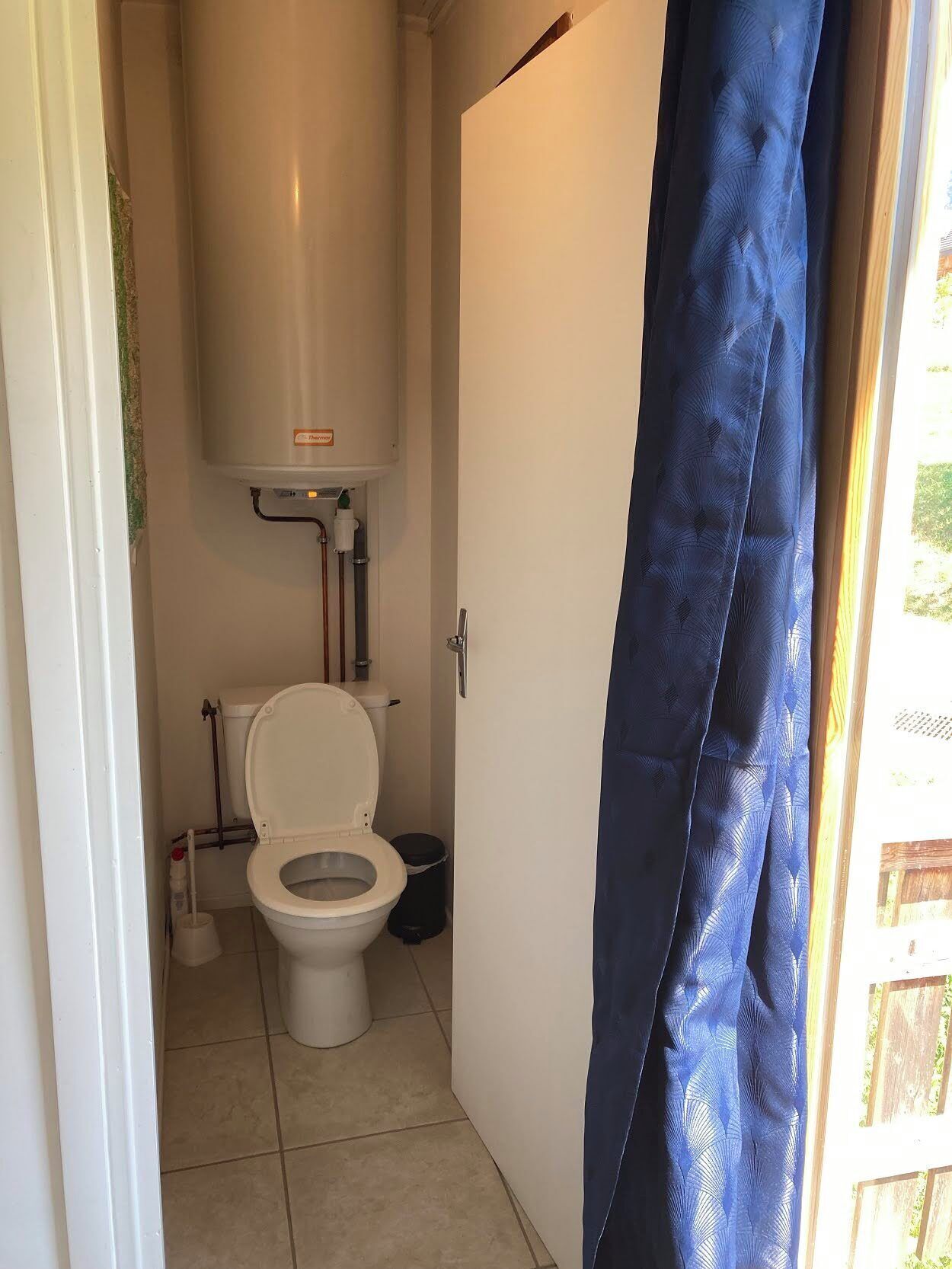 Une petite salle de bain compacte, équipée de toilettes, d’un lavabo blanc et d’un rideau de douche.