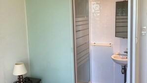 A bedroom with a bed, a nightstand, a lamp, a bathroom with a sink and mirror, and a sliding door.