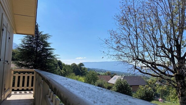 A balcony with a view of a distant landscape, a wooden fence, and a tree.