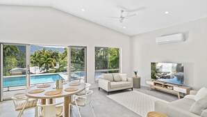 A spacious living area with a pool view, a flat-screen TV, and a ceiling fan. - Belle Escapes Sea La Vie (Trinity Beach)