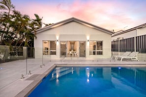 A modern house with a swimming pool, glass doors, and a patio with lounge chairs.