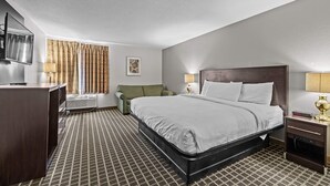 A hotel room with a bed, a desk, a chair, a TV, and a lamp.