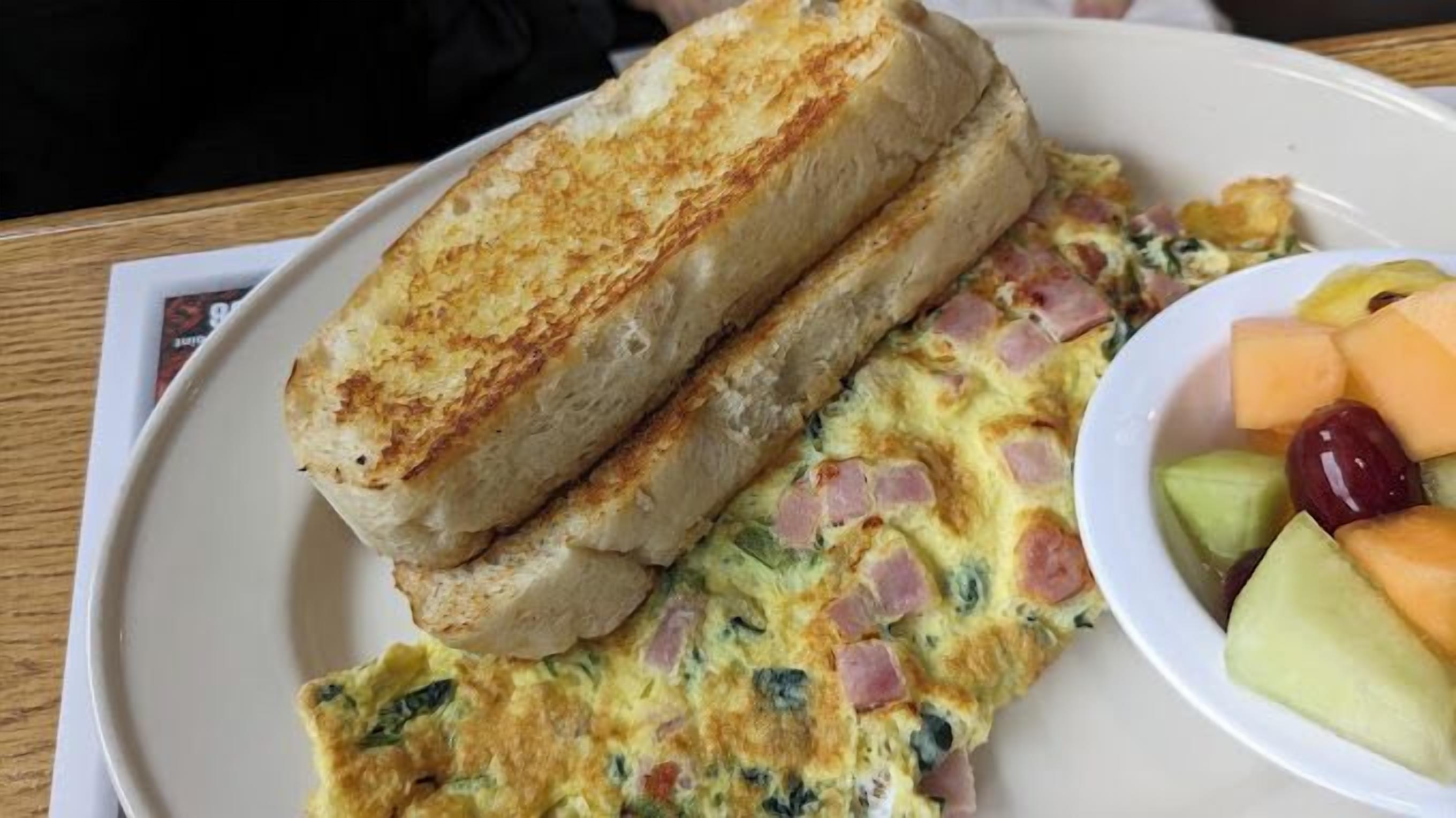 A plate with grilled toast, a vegetable omelette, and a side of melon and grapes.