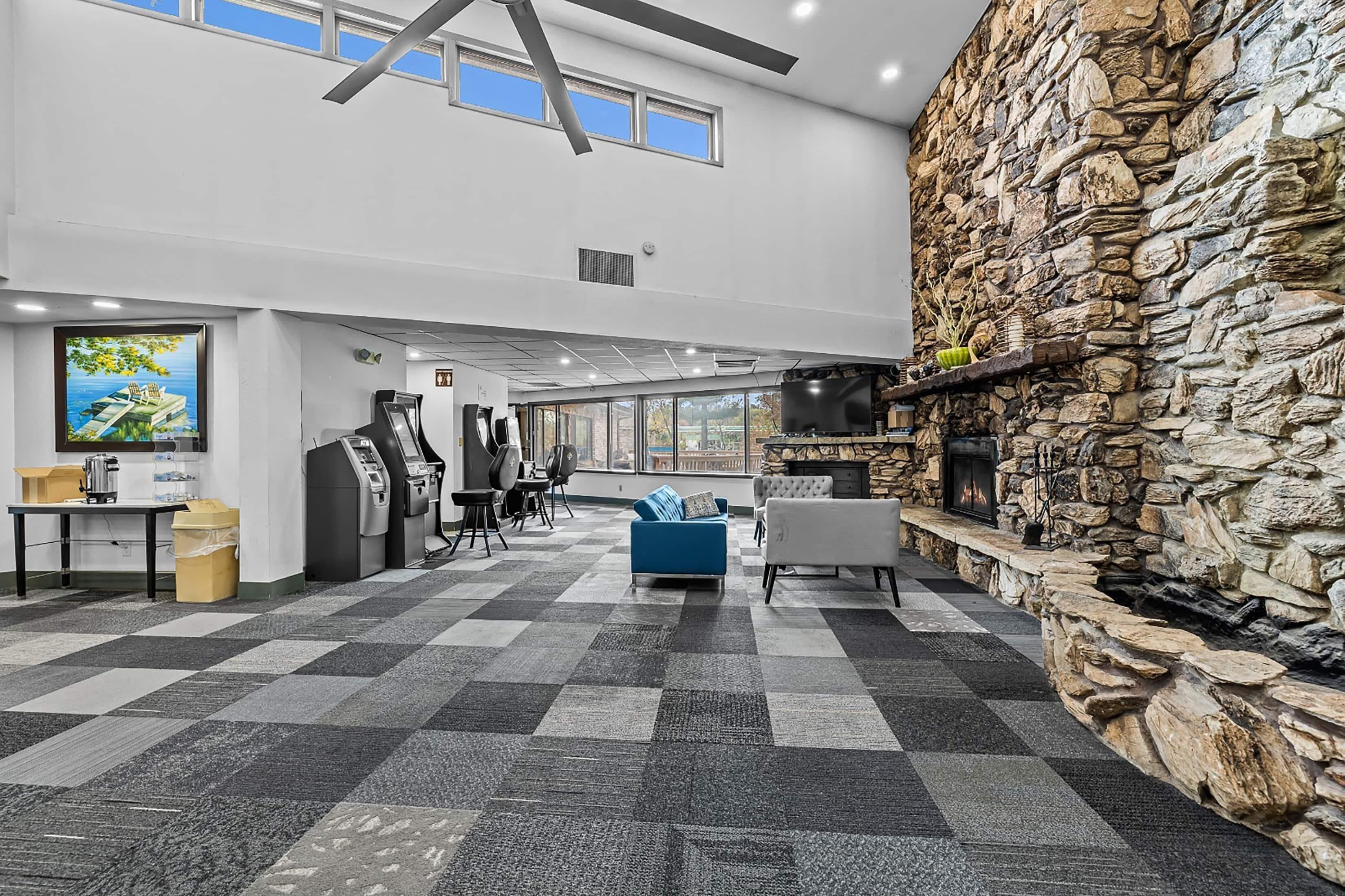 A spacious lobby with a checkered floor, a stone wall with a fireplace, a large window, and a seating area with a blue sofa.