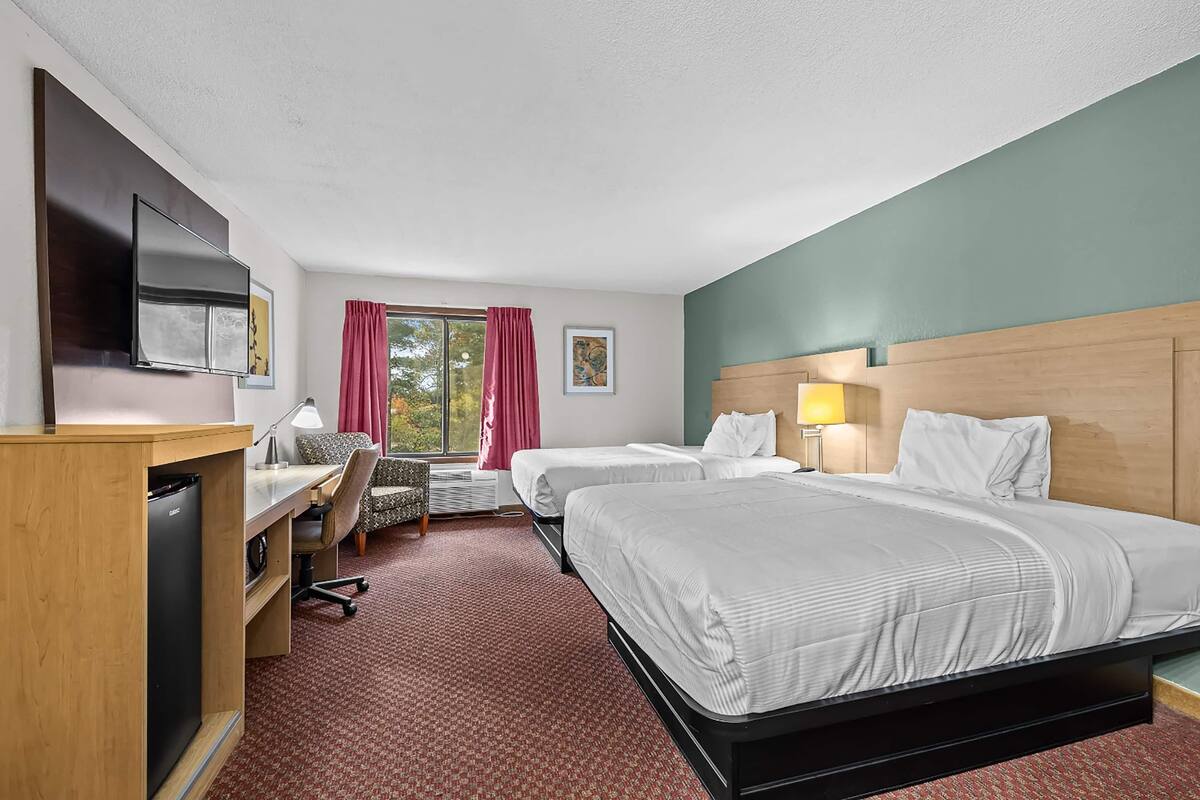 Habitación de hotel con dos camas, un escritorio, una silla, un televisor y una ventana con cortinas.