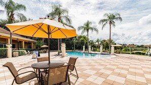 A poolside area with a checkered tile floor, a round table with chairs, and a large umbrella. - 2BR Encantada Townhome with Jacuzzi (Kissimmee)