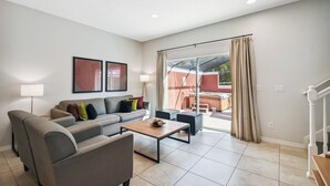A modern living room with a sofa, armchairs, a coffee table, and a large sliding glass door leading to an outdoor area. - 2BR Encantada Townhome with Jacuzzi (Kissimmee)
