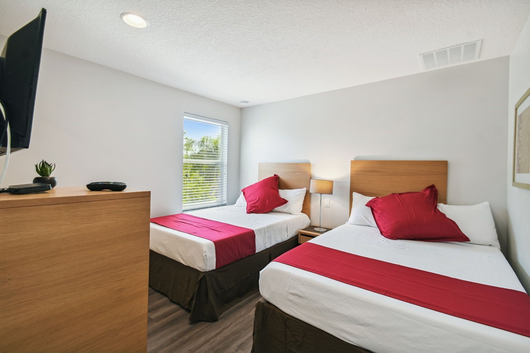 A hotel room with two beds, a desk, and a window with blinds.