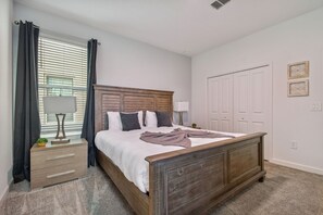 Een slaapkamer met een houten bed, nachtkastje met lamp, een dressoir en een raam met gordijnen.