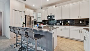 Una cocina moderna con armarios blancos, electrodomésticos de acero inoxidable y una barra con taburetes.