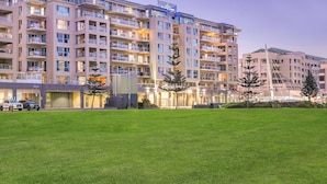 A multi-story hotel with balconies, a parking area, and a well-maintained lawn.