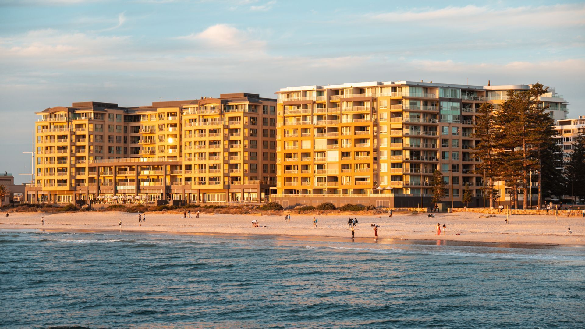 Un hôtel en bord de mer, avec plusieurs étages, des balcons et une plage de sable au premier plan.
