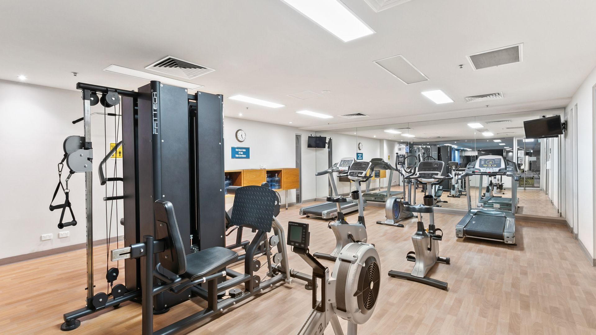 A gym with various exercise machines, a wall clock, and a water dispenser.