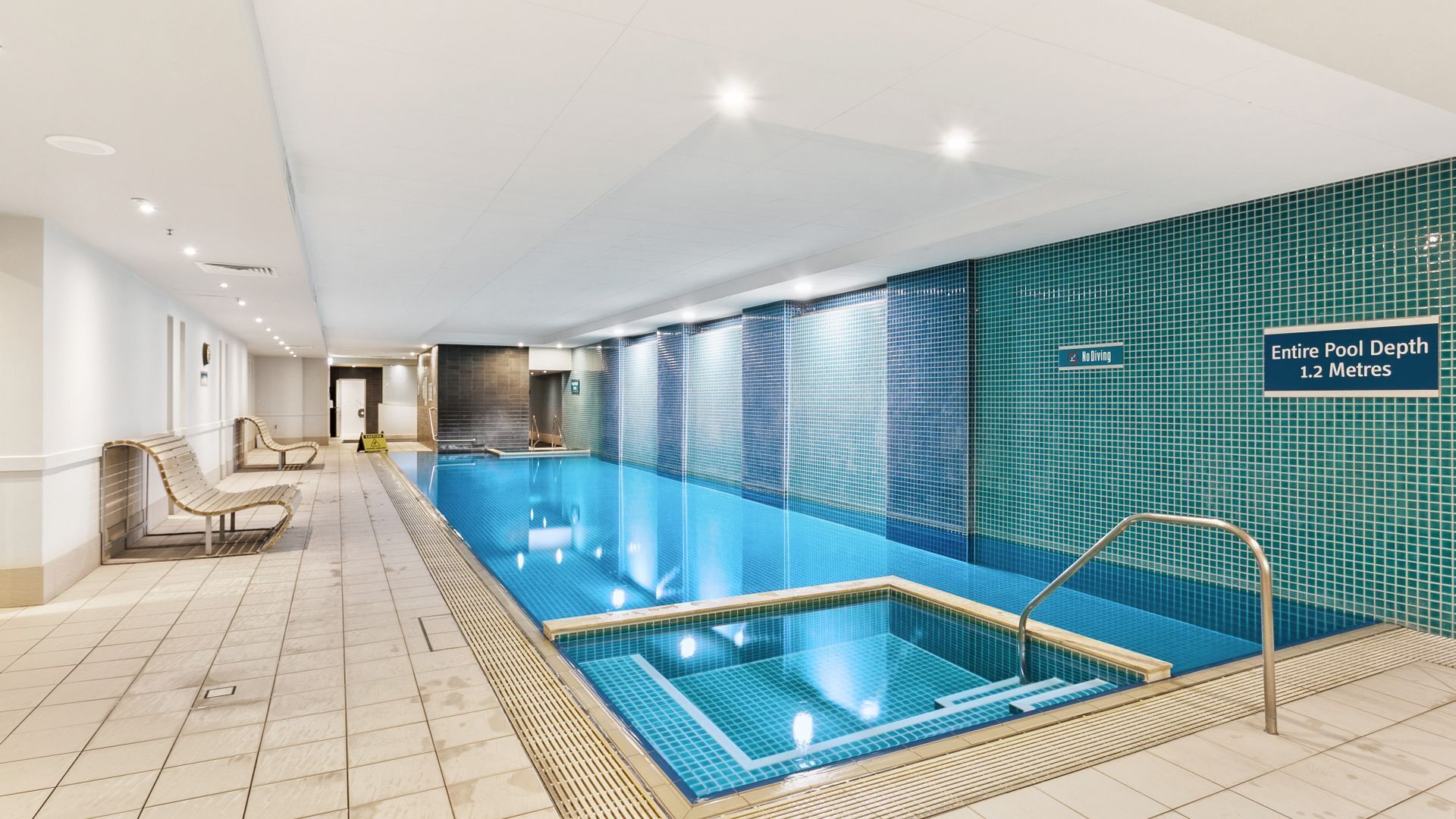 Une piscine d’une profondeur de 1,2 mètre, avec un panneau indiquant qu’il est interdit de plonger, et un mur recouvert de carreaux.