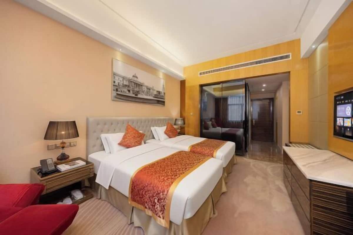 A hotel room with a bed, a desk, a chair, a TV, and a door leading to a bathroom.