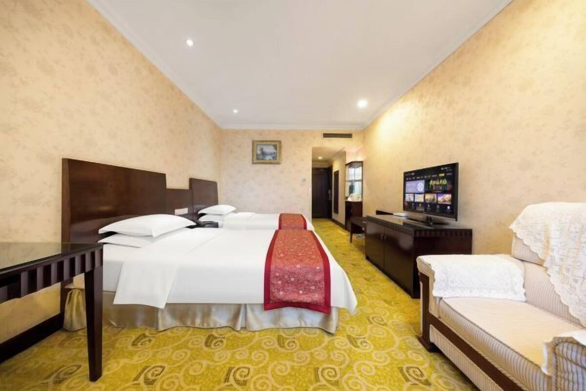 A hotel room with two beds, a desk, a television, and a sofa.