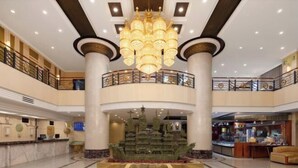 A hotel lobby with a grand chandelier, marble flooring, a reception desk, and a decorative fountain.