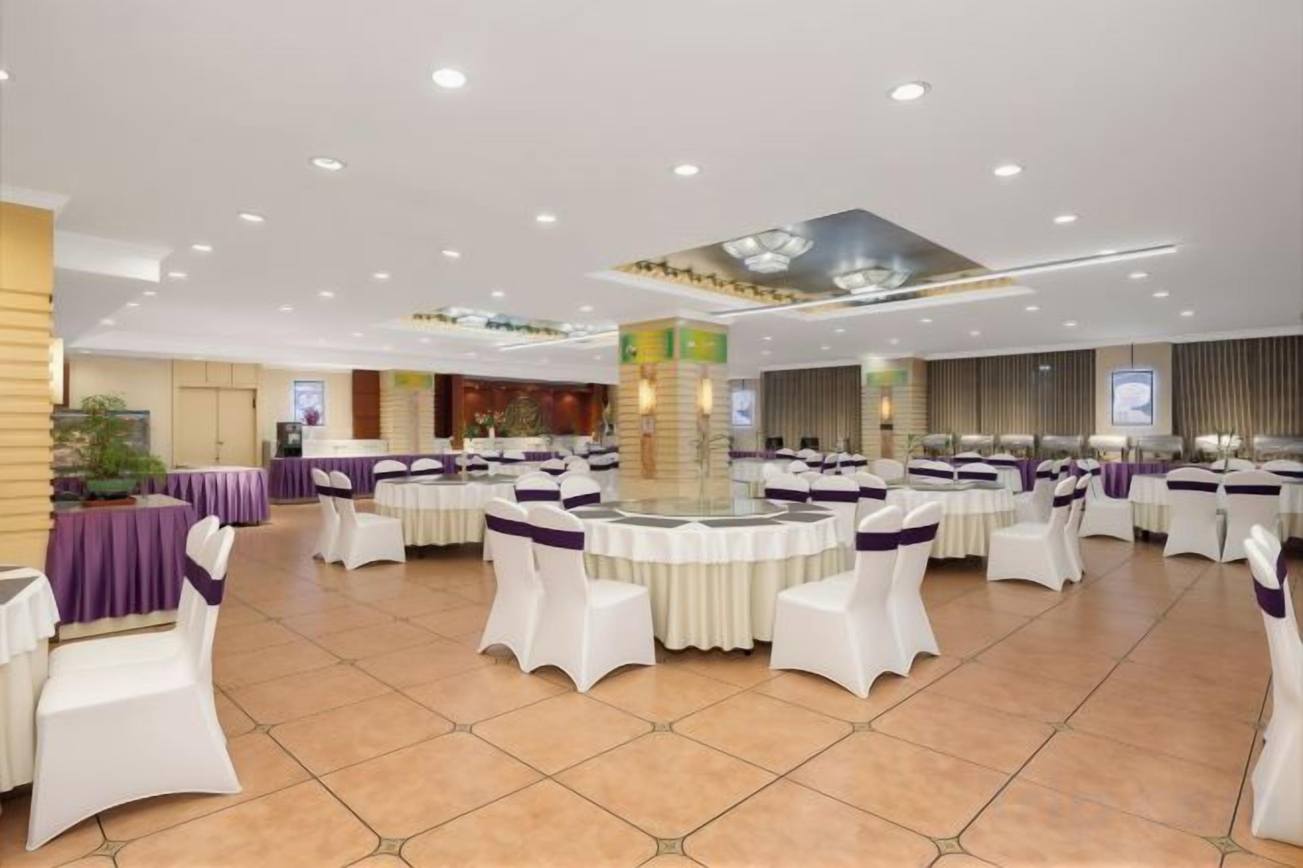 A banquet hall with round tables and white chairs, a stage, and a large screen.