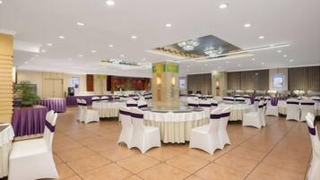 A banquet hall with round tables and white chairs, a stage, and a large screen.