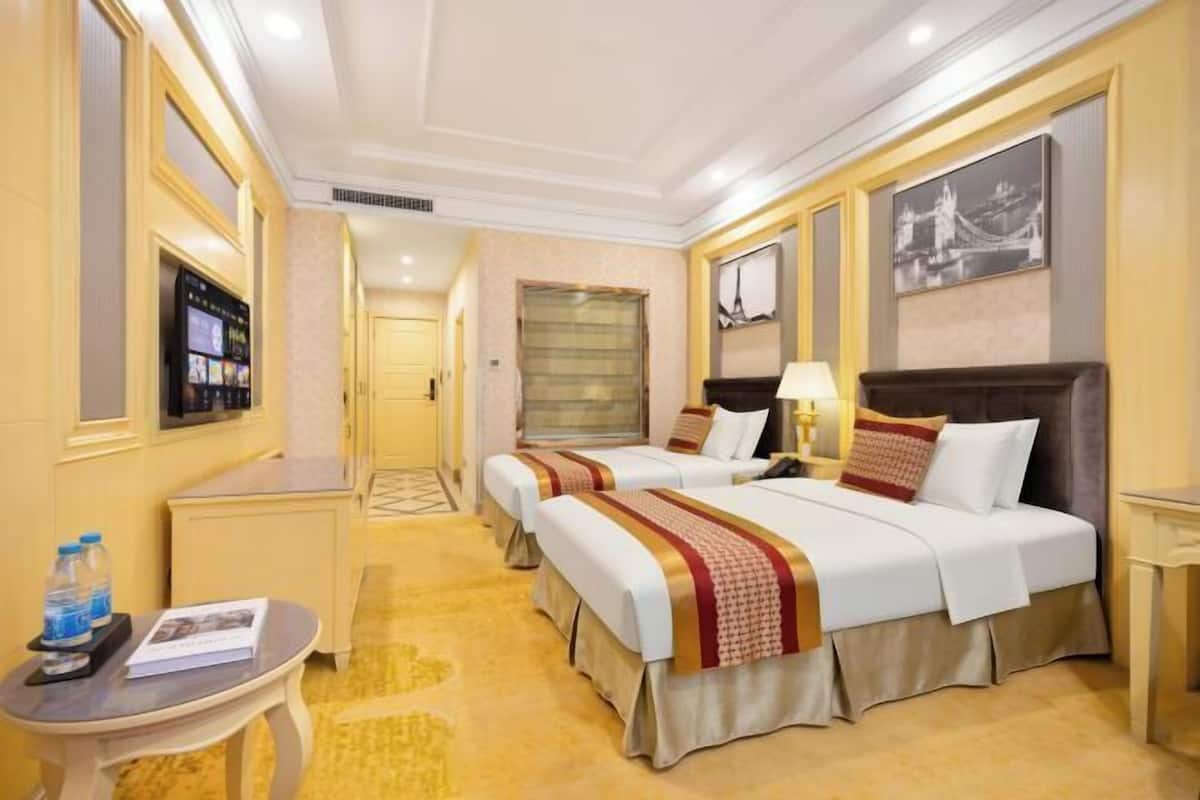A hotel room with two beds, a TV, a desk, a lamp, and a framed picture on the wall.