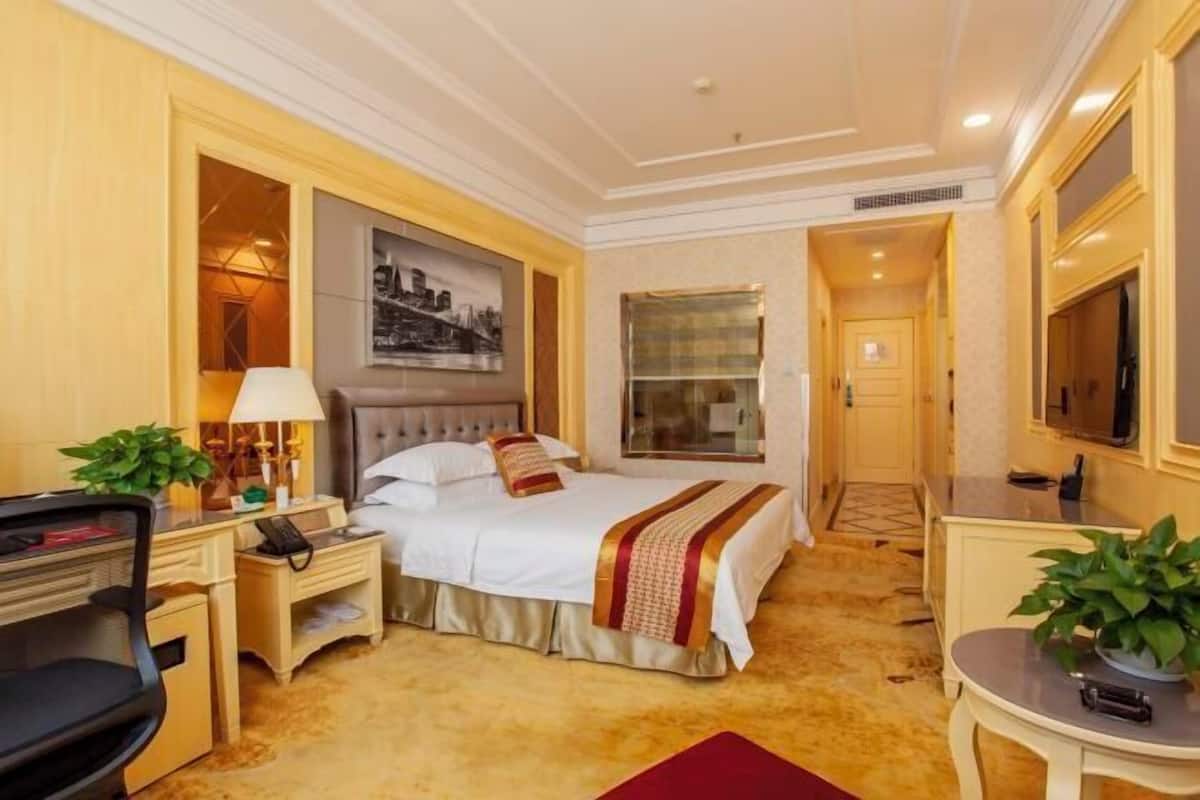 A hotel room with a bed, bedside table, lamp, chair, desk, and a TV.