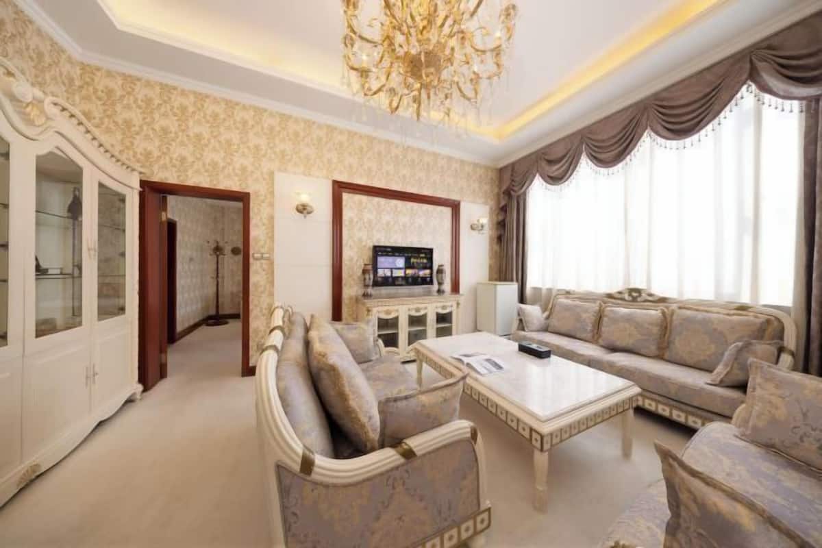 A spacious living room with a sofa set, a coffee table, a television, and a chandelier.