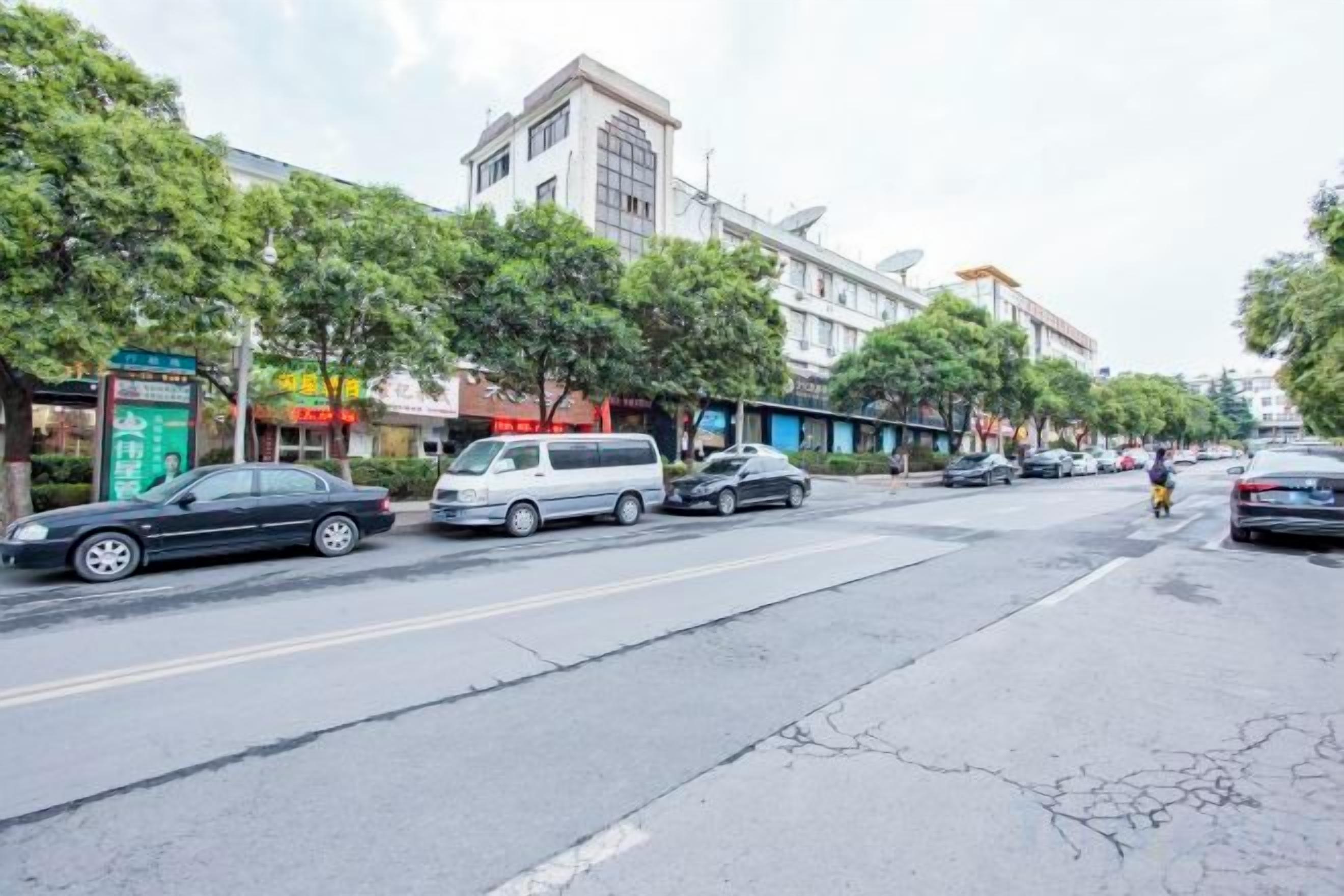 A street with parked cars, trees, and buildings.