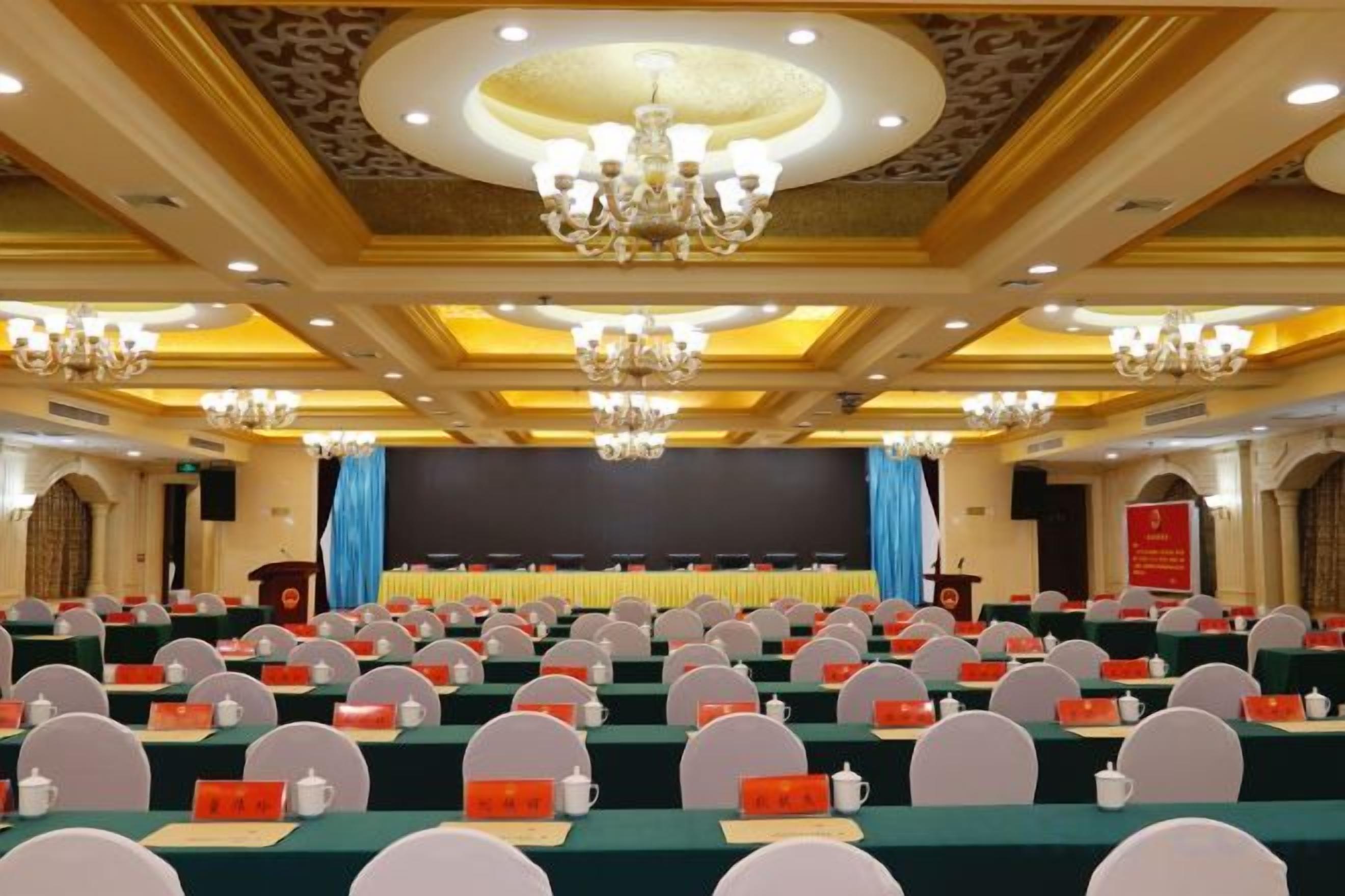 A conference room with rows of tables, chairs, and a stage with a screen.