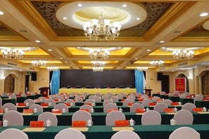 A conference room with rows of tables, chairs, and a stage with a screen. - Qingping Hotel (Xinmi)