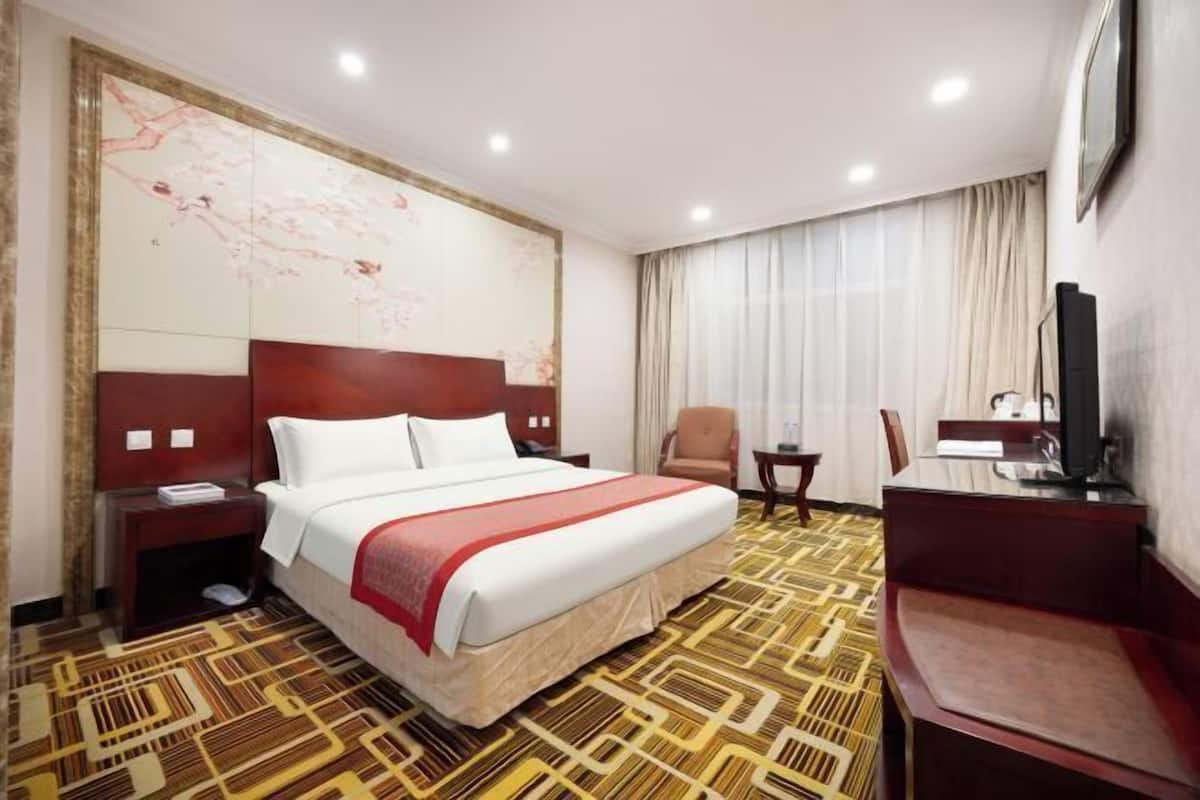 A hotel room with a large bed, a desk, a chair, a television, and a map on the wall.