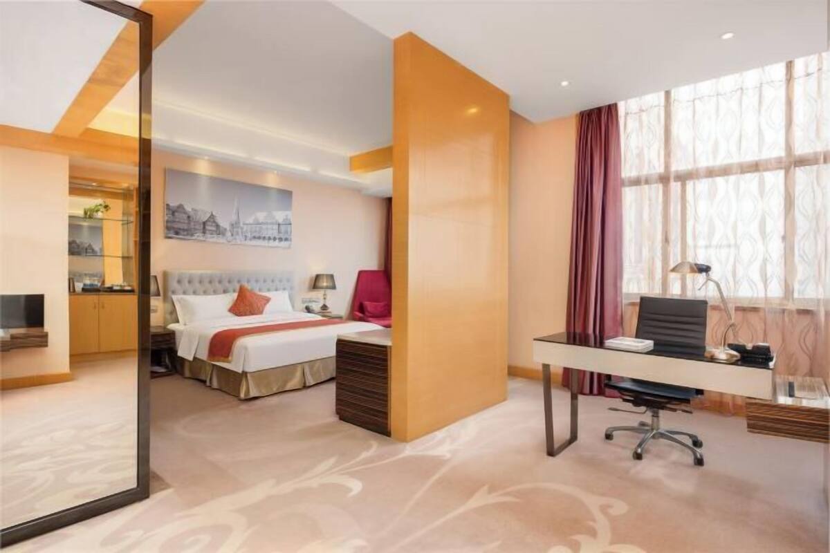 A hotel room with a bed, desk, and large window.