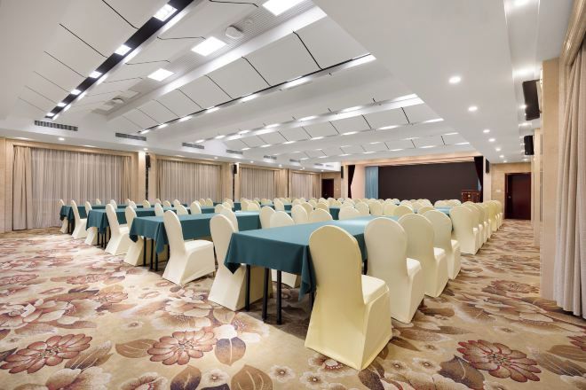 A conference room with rows of tables and chairs, a carpeted floor, and a stage area.