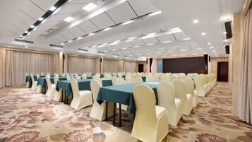 A conference room with rows of tables and chairs, a carpeted floor, and a stage area.