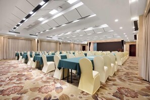 A conference room with rows of tables and chairs, a carpeted floor, and a stage area. - Qingping Hotel (Xinmi)