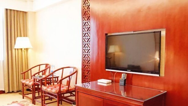 A hotel room with a TV, wooden furniture, and a patterned wall. - Qingping Hotel (Xinmi)