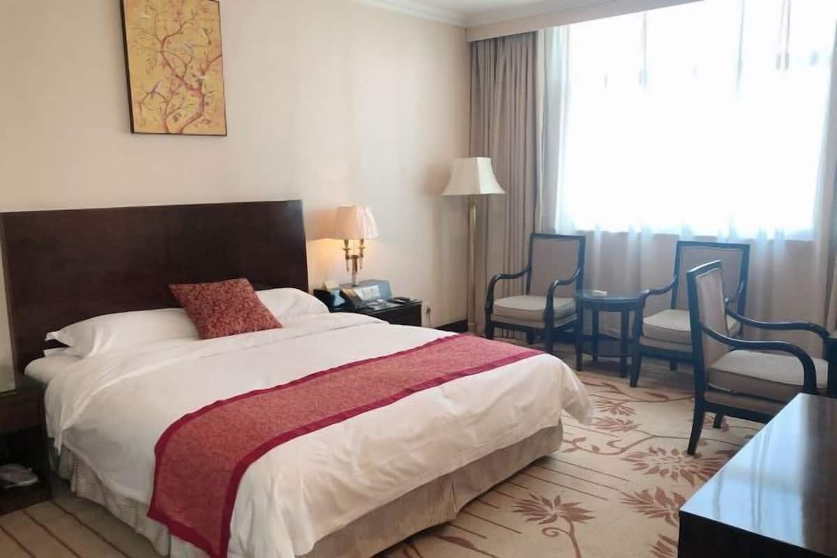 A hotel room with a large bed, a nightstand, a desk, two chairs, a lamp, and a window with curtains.