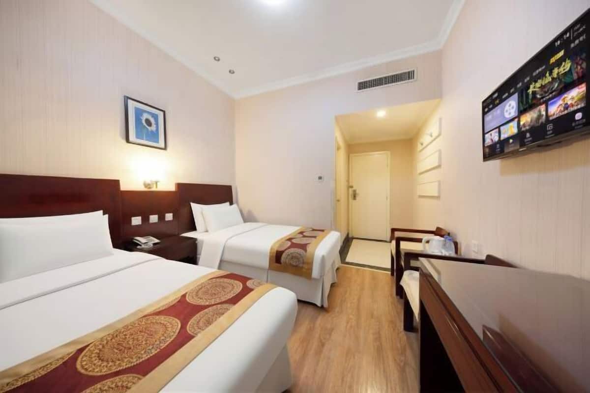 A hotel room with two beds, a TV on the wall, and a wooden floor.