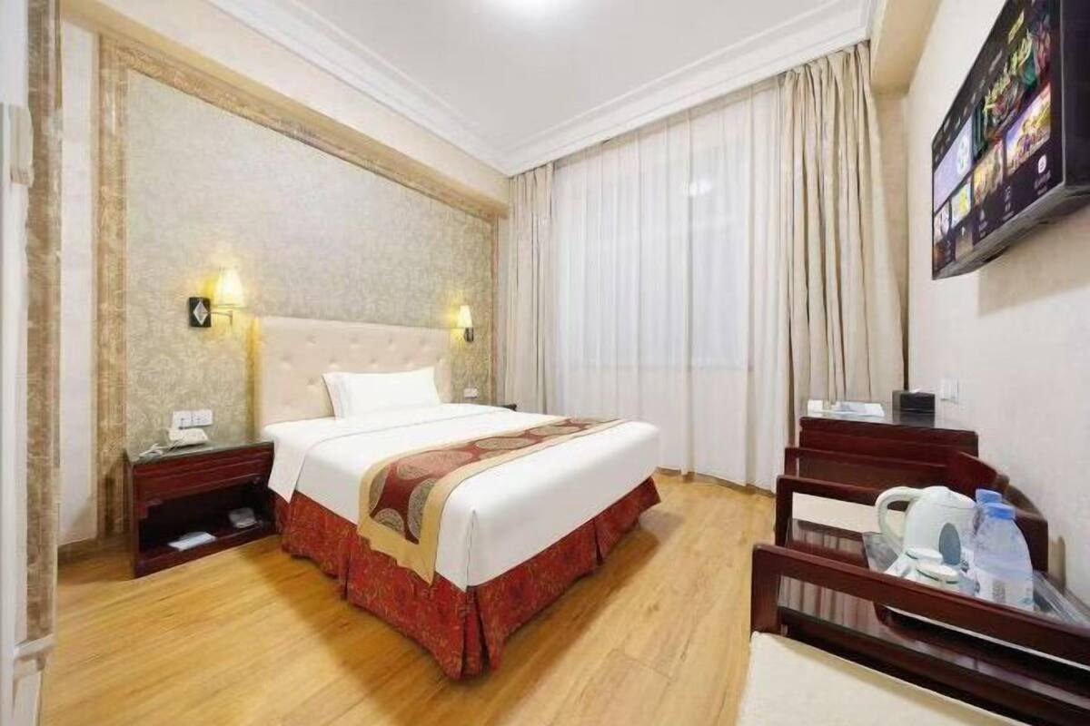 A hotel room with a bed, bedside tables, a TV, and curtains.
