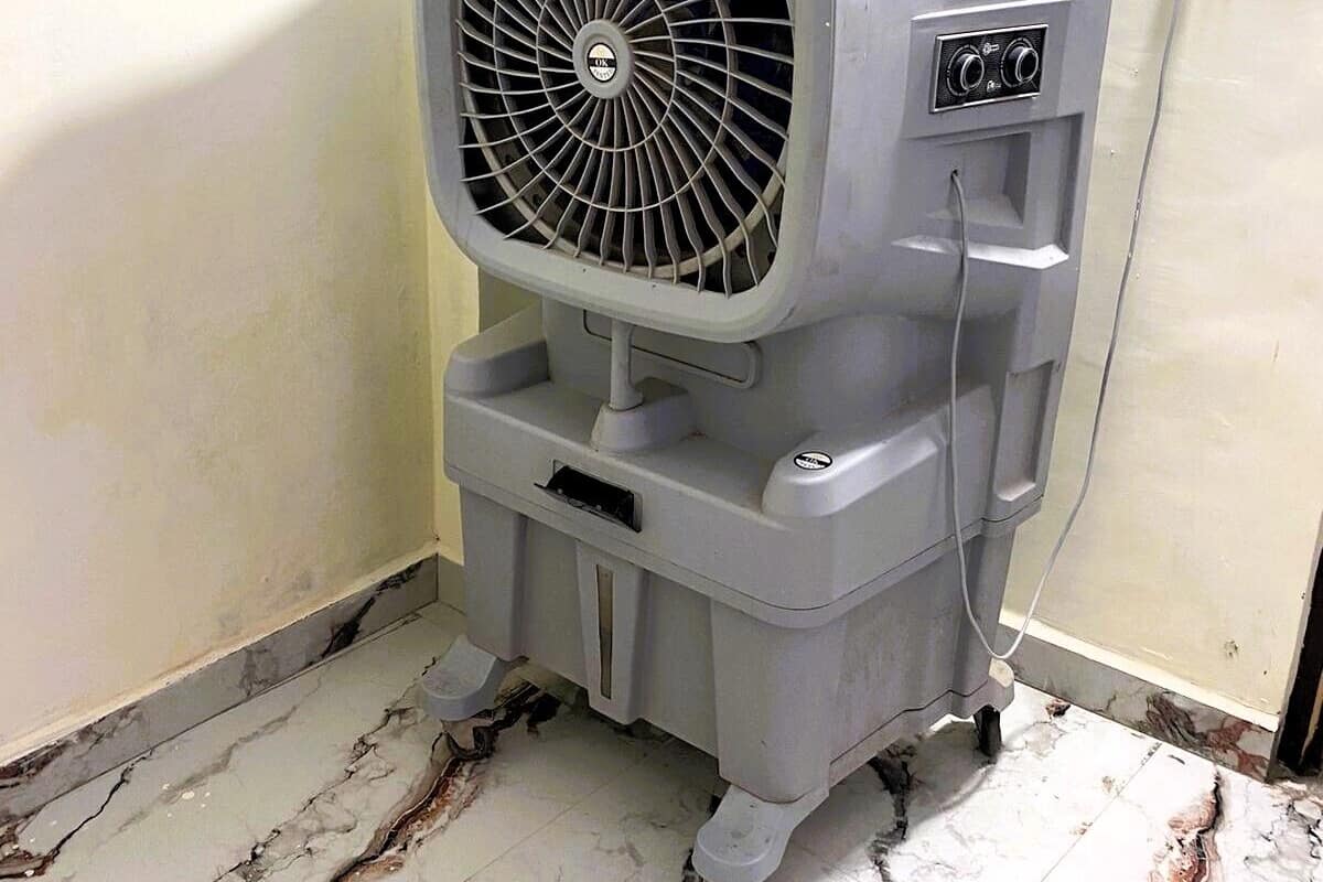 Un climatiseur portatif est placé dans un coin d’une pièce dont le sol est carrelé.